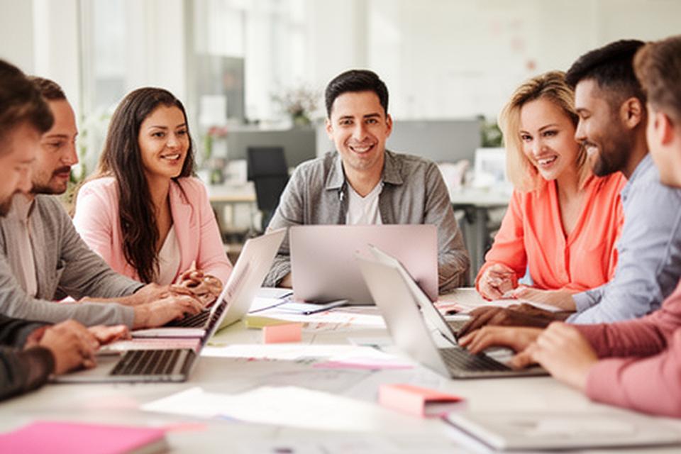Diverse professionals collaborating around a bright office table with laptops and interview notes